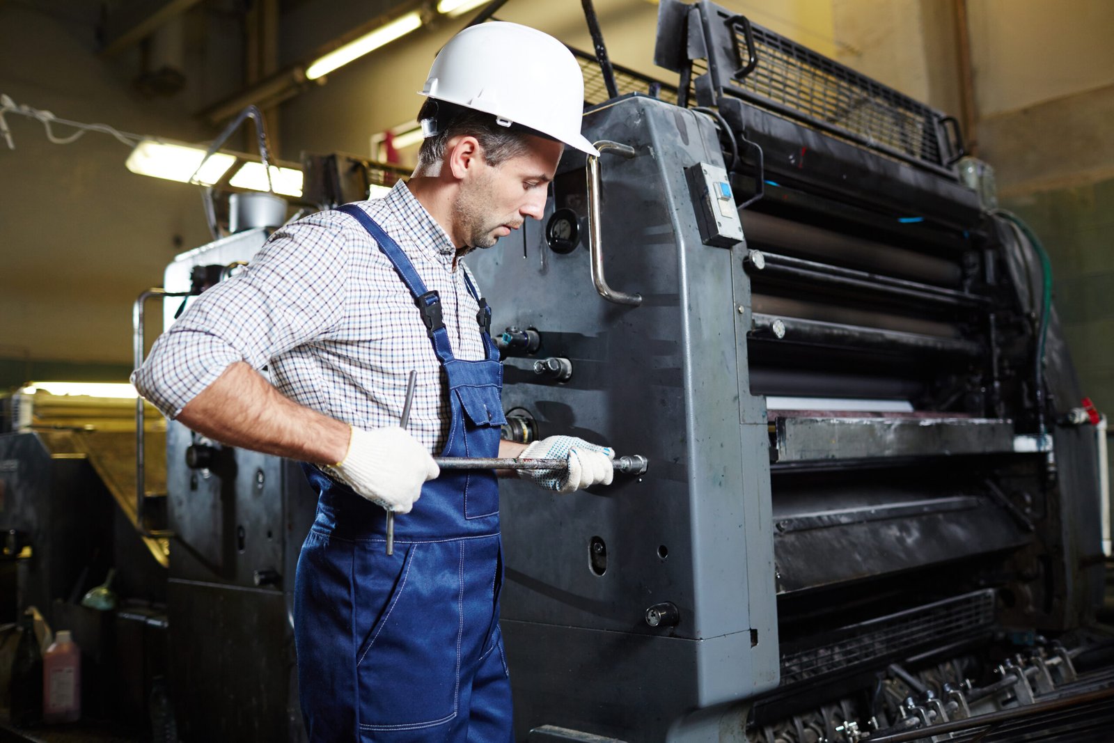 Worker with handtool standing by huge machine and checking its working condition